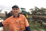 Robin Schaefer amidst the busy seeding period A man in an orange work shirt and a cap stands in front of a tractor.