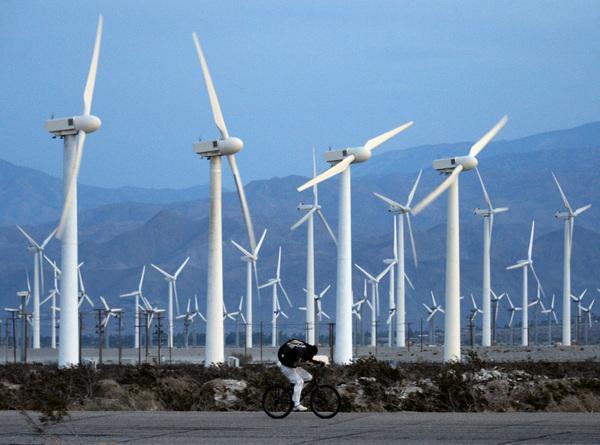 PALM SPRINGS, CA - MARCH 27: A man rids his bike against the win as giant wind turbines are powered by strong winds at sunset on March 27, 2013 in Palm Springs, California. According to reports, California continues to lead the nation in green technology and has the lowest greenhouse gas emissions per capita, even with a growing economy and population. (Photo by Kevork Djansezian/Getty Images)