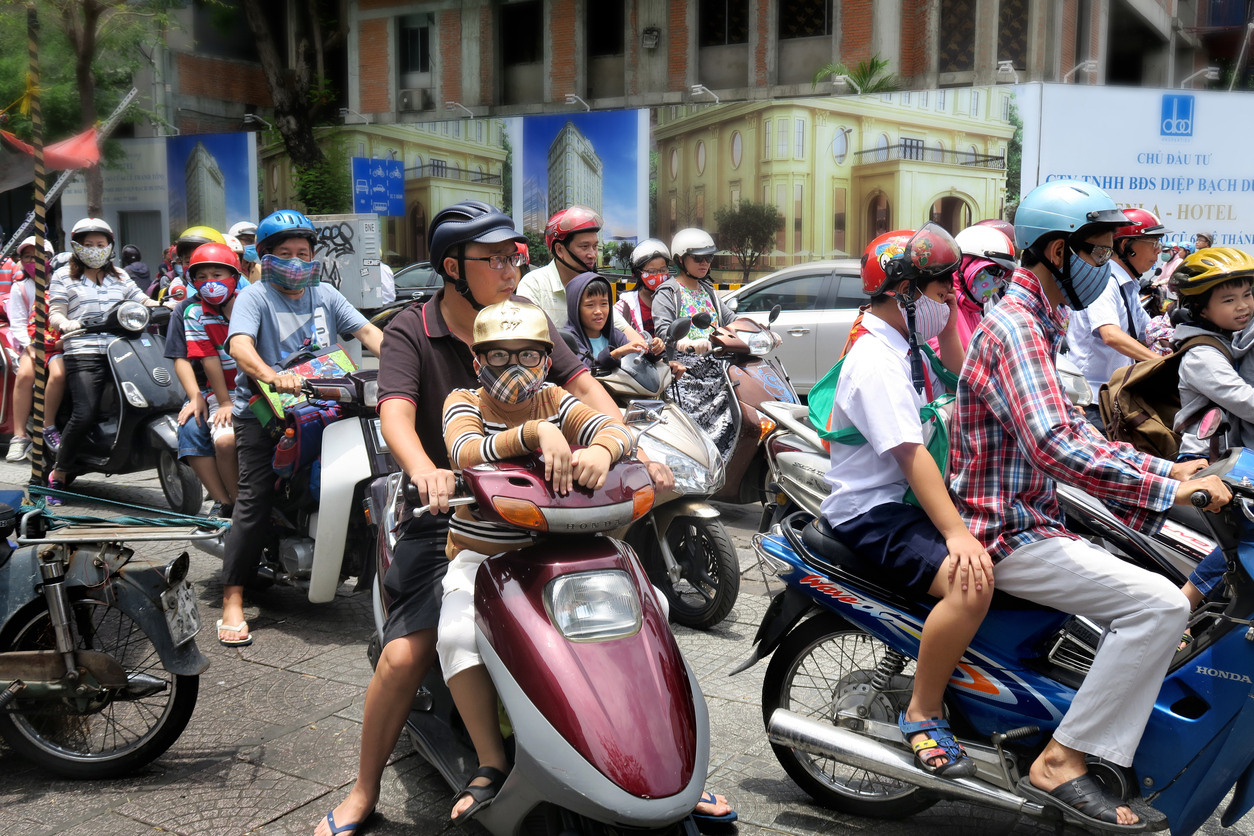 parents picking up their children from school and driving them home on motor scooters in downtown Ho Chi Minh City, Vietnam- many of them are wearing masks to deal with the air pollution