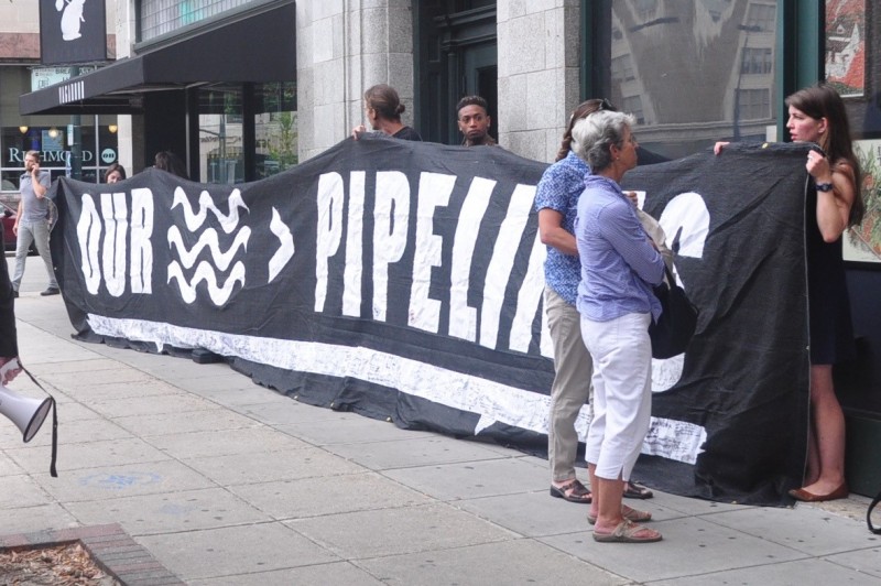 Protesters against new natural gas pipelines proposed across Virginia unfurled a banner at Clean Water Forum in Richmond, where both major-party candidates spoke on environmental issues. (Whitney Pipkin)