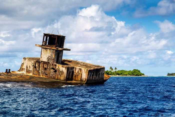 A rusty shipwreck in Enetewak Atoll with an island behind.